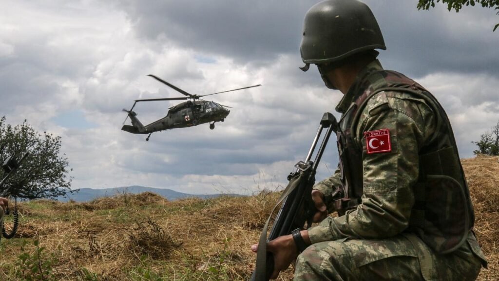 Turkish soldier kneeling with a rifle as a UH-60 Black Hawk lands